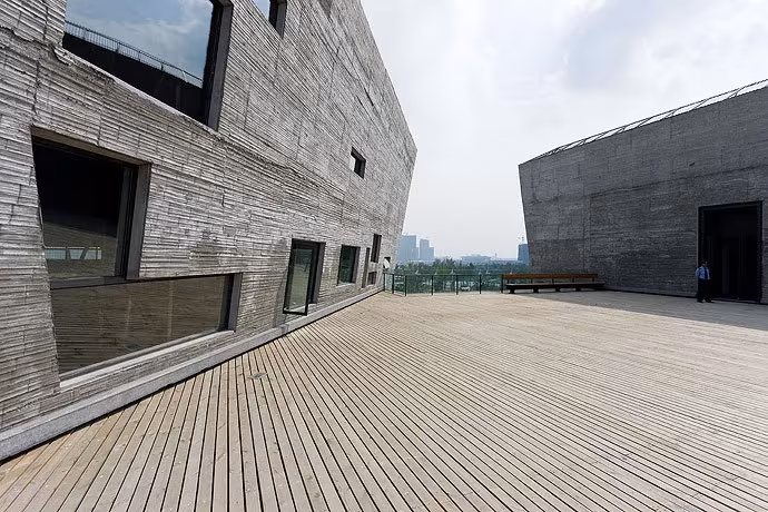 Terraza de madera junto al muro de hormigón y ladrillo del Museo de Ningbo con ventanas de formas dispares