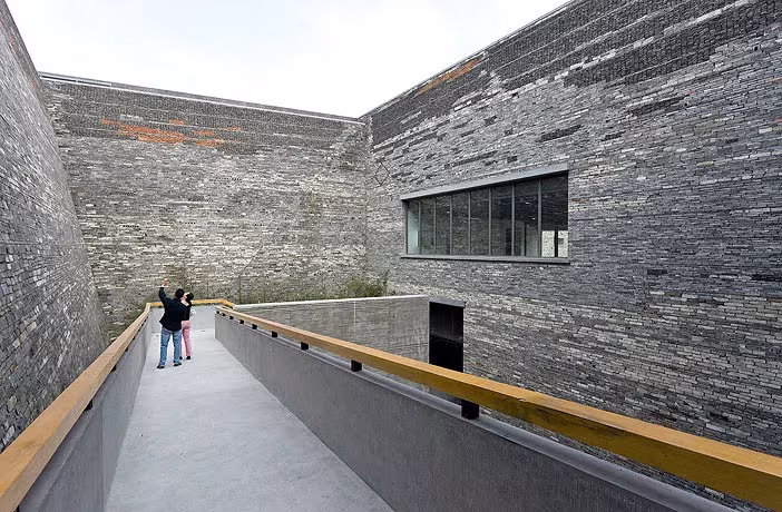 Rampa con pasamanos amarillo entre muros de ladrillo y piedra recuperados del Museo de Ningbo de Wang Shu