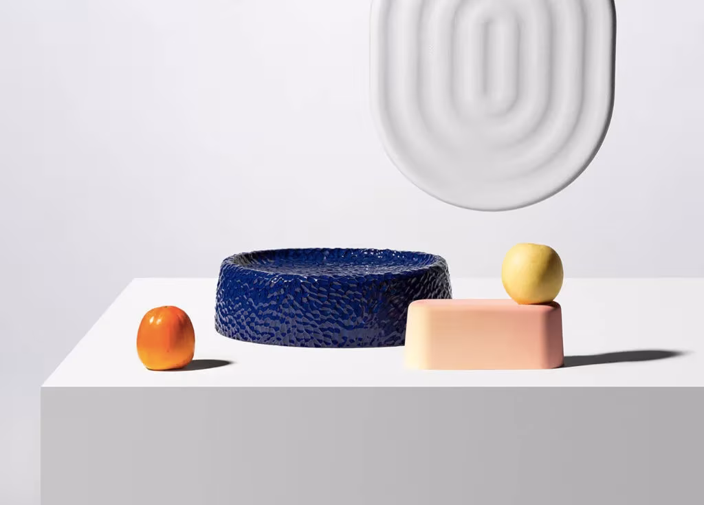 Piezas cerámicas de Dimitri Bähler en azul, rosa y blanco con relieves sobre un pedestal junto a frutas