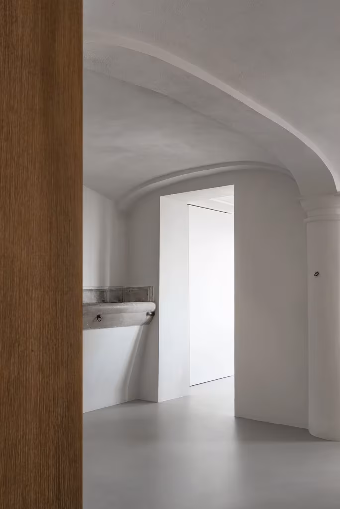 Estancia abovedada blanca de la Casa AG en Milán vista tras un panel de madera oscura