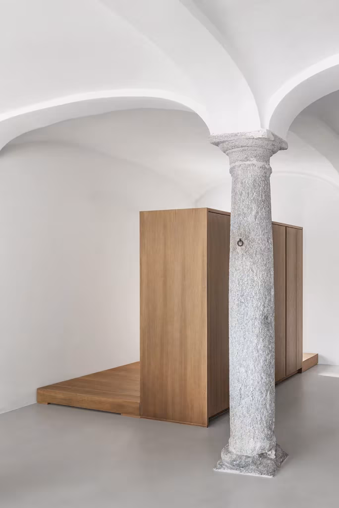 Columna antigua de piedra bajo bóvedas de arista junto a un mueble de madera en la Casa AG