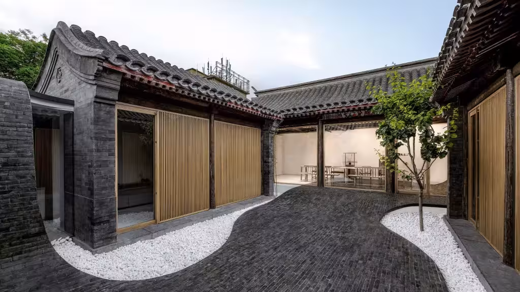 Patio del siheyuan de Arch Studio con suelo de ladrillo ondulado, banda de guijarros blancos y un árbol