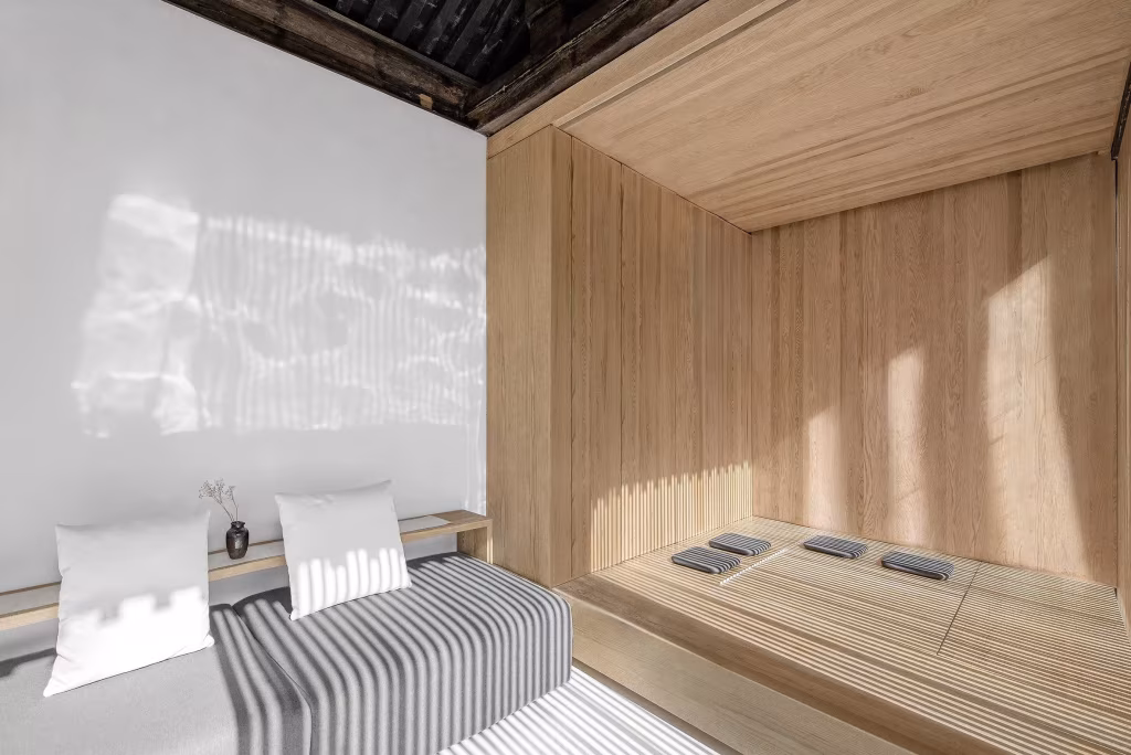 Estancia blanca con banco tapizado a rayas y plataforma de madera con cojines de suelo en la casa de Arch Studio