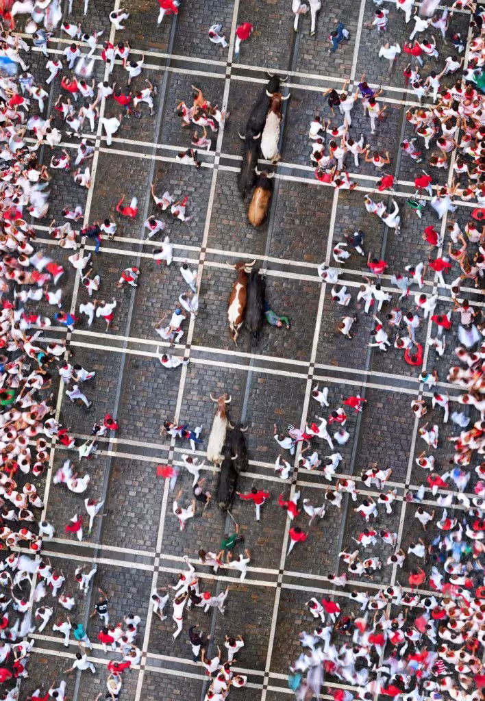 Vista cenital de corredores vestidos de blanco y rojo junto a toros en un encierro de San Fermín