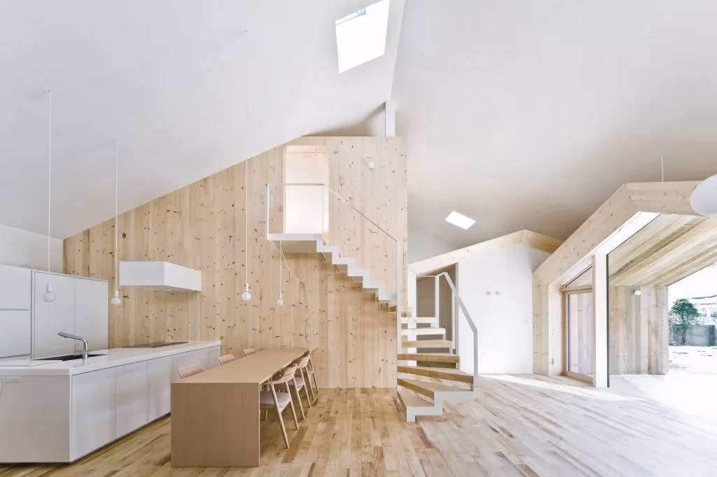 Interior de la House K de Yoshichika Takagi con paredes de madera clara, escalera y cocina blanca bajo cubierta inclinada