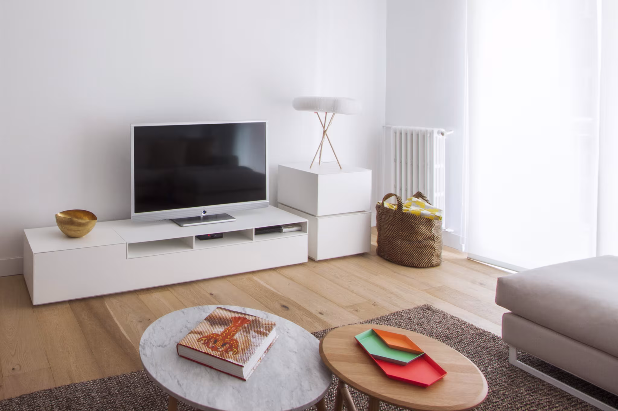 Salón pequeño con mueble bajo blanco y televisor, mesas de centro redondas y parqué en un proyecto de Castellana