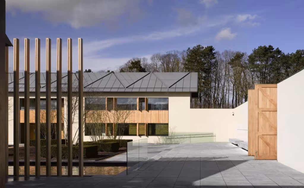 Patio de Windmill Hill con lámina de agua, pilares de madera y muros blancos ante un edificio de cubierta gris