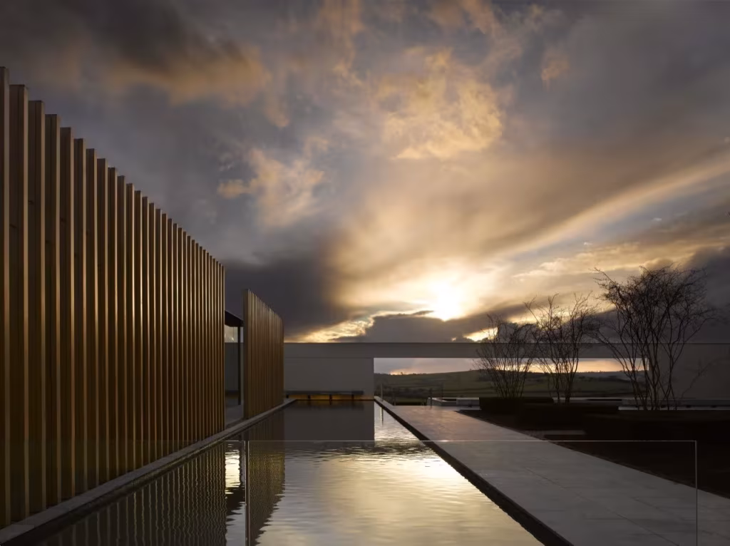 Estanque alargado entre pilares de madera de Windmill Hill reflejando un cielo de nubes al atardecer