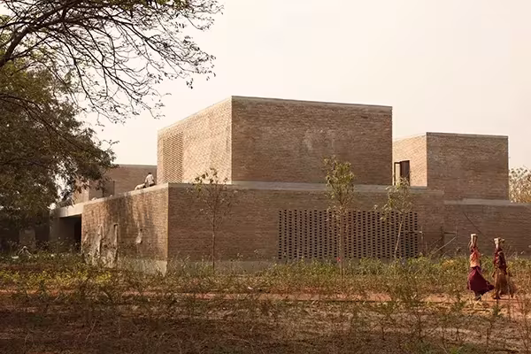 Volúmenes de tierra apisonada con celosía de ladrillo en el paisaje, obra de Studio Mumbai