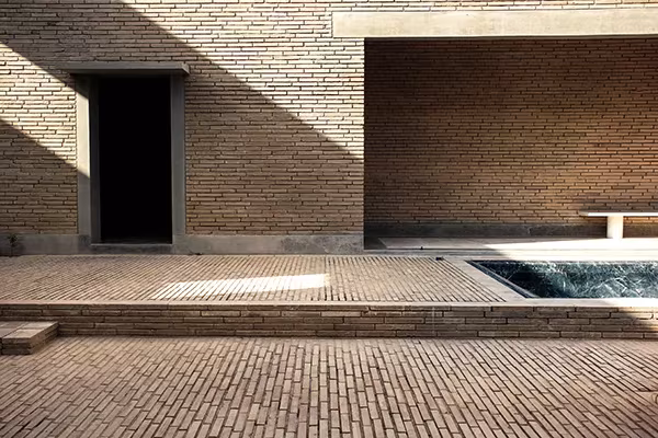 Patio de ladrillo con estanque y fachada de ladrillo con huecos en una obra de Studio Mumbai