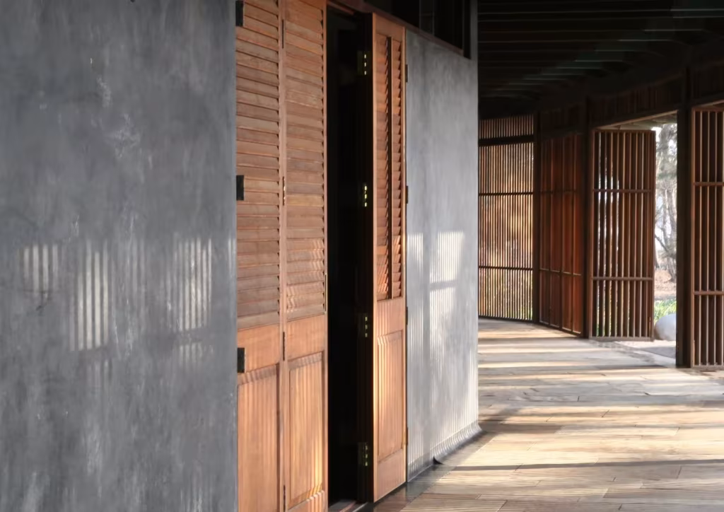 Detalle de contraventanas de madera junto a un muro de cal gris en una obra de Studio Mumbai, Bijoy Jain
