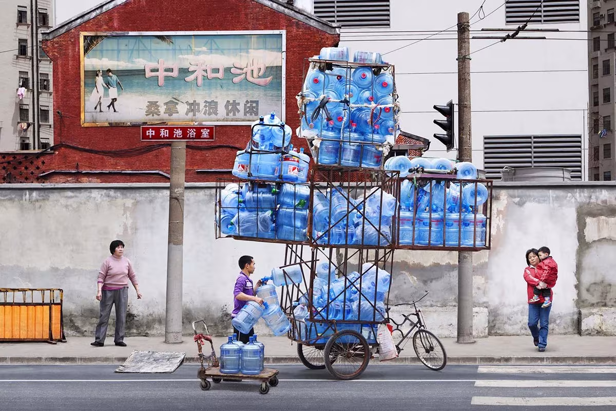 Triciclo cargado con una torre de garrafas de agua azules en una calle de Shanghái