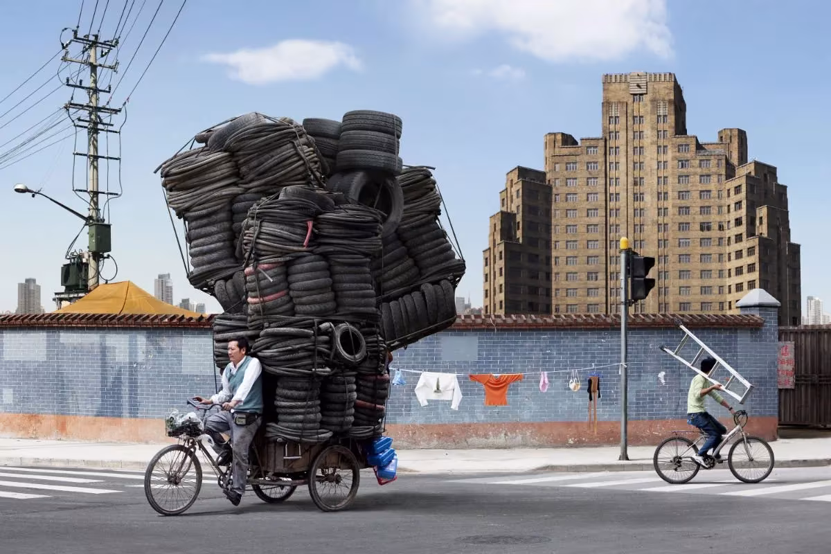 Triciclo de carga con una torre gigante de neumáticos usados cruzando una calle de Shanghái
