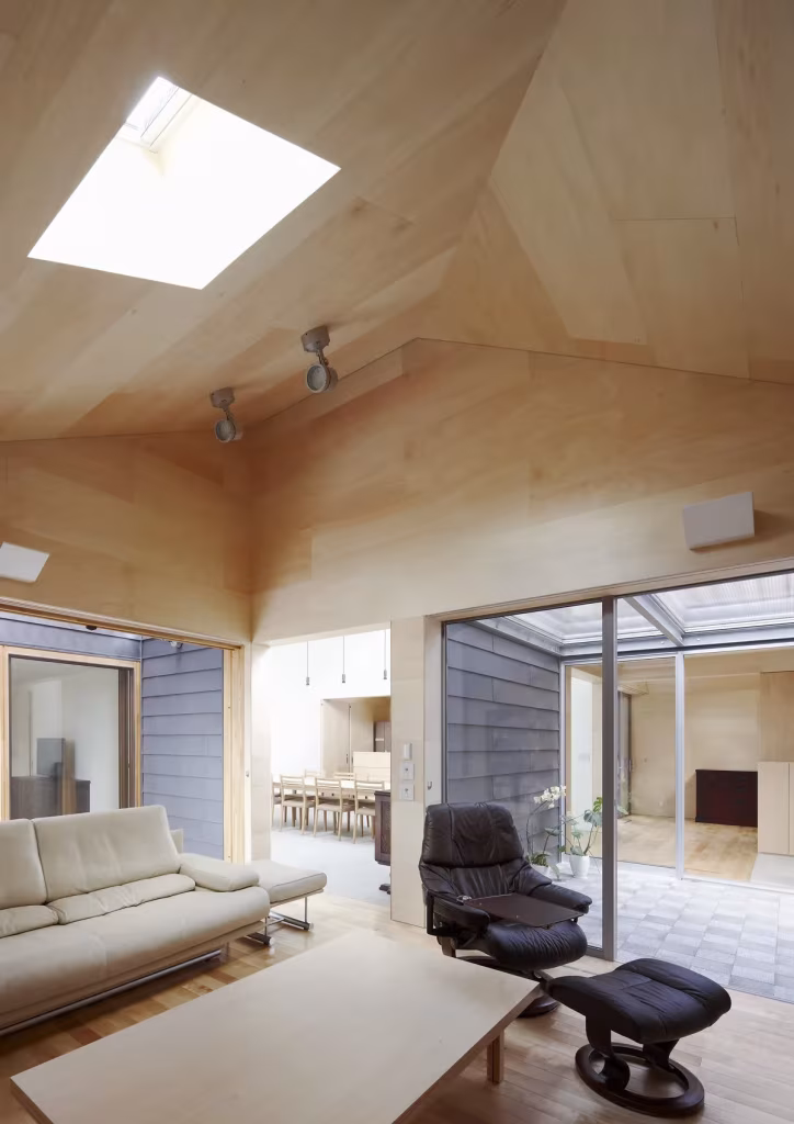 Sala con techo facetado de madera clara y lucernario abierta a un patio en la Casa Yagiyama de Kazuya Saito