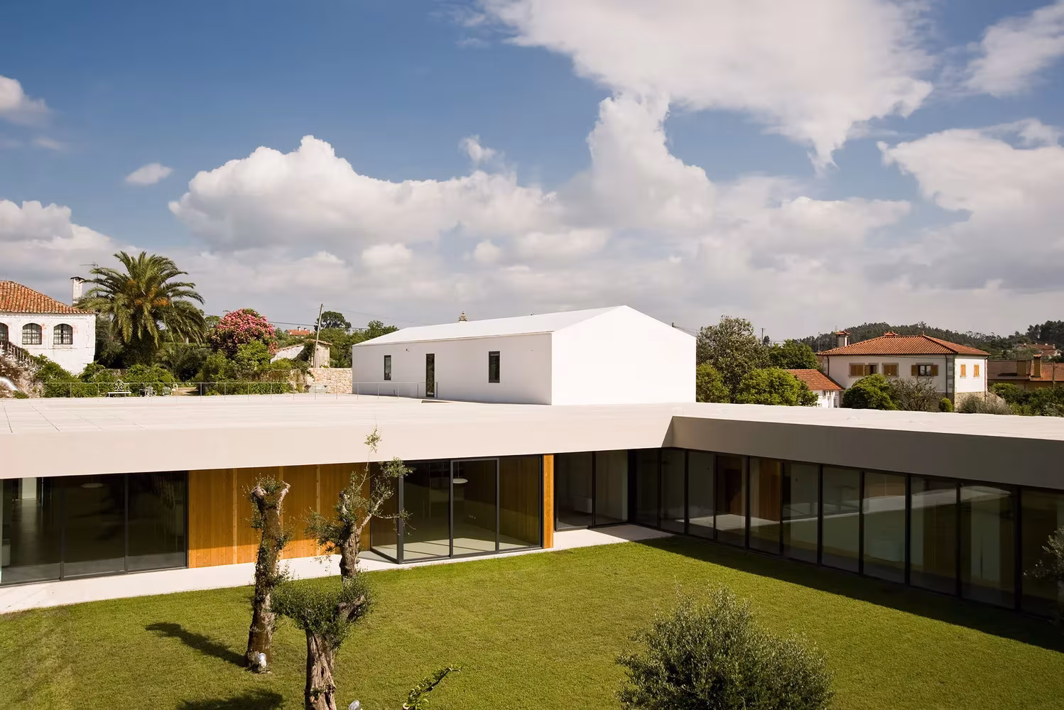 Patio de césped con olivos y galería acristalada en la Casa de Magalhães, con una casa blanca al fondo