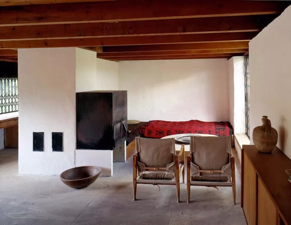 Dormitorio con chimenea de obra blanca, butacas de cuero y cama con manta roja en la casa de Roland Rainer