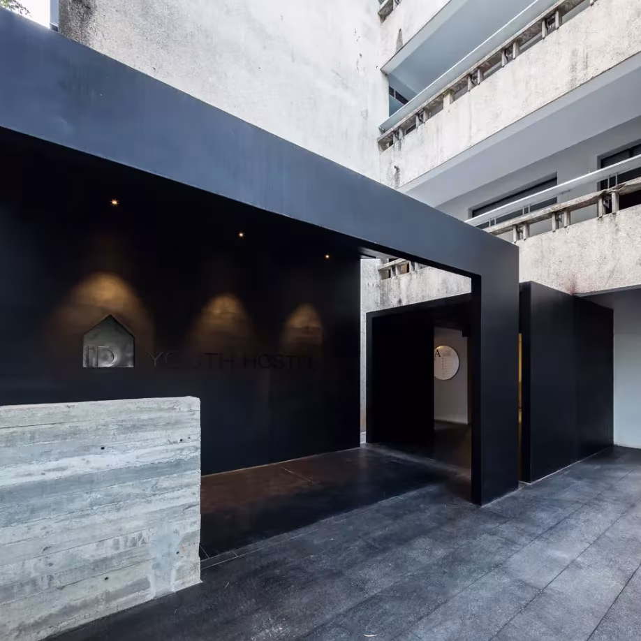 Recepción del albergue iD Town con portal negro, mostrador de hormigón encofrado y fachada del edificio original