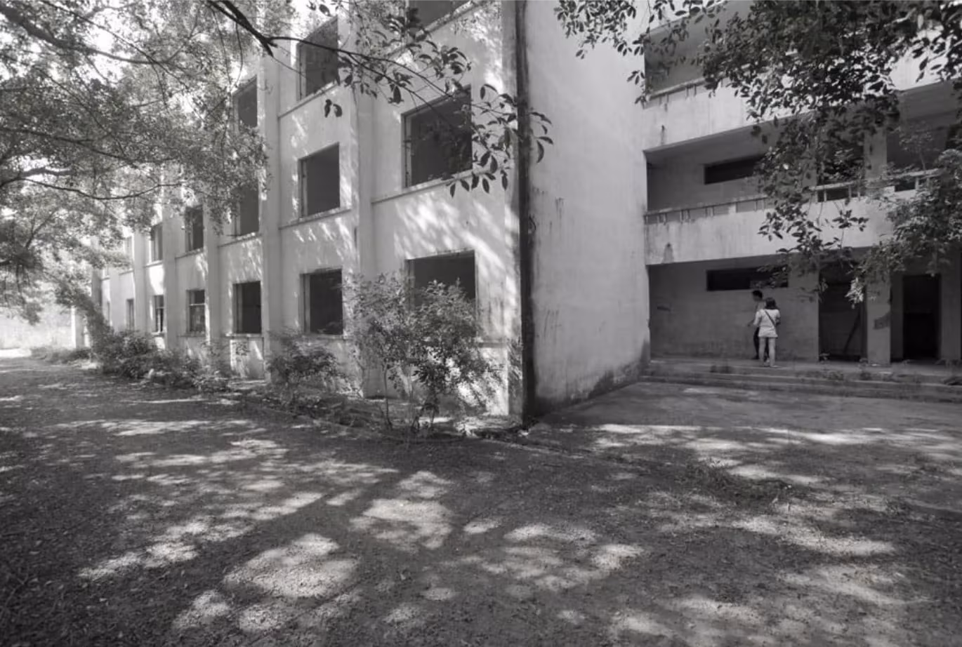 Fachada original en blanco y negro del dormitorio industrial de Shenzhen bajo los árboles, antes de la reconversión