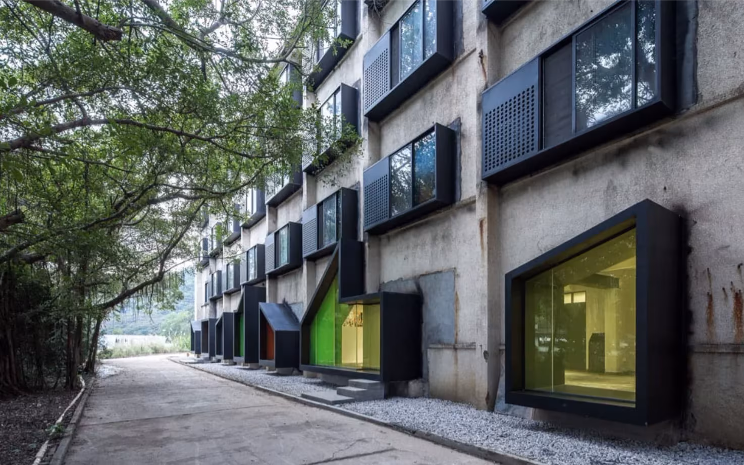 Fachada de hormigón del albergue iD Town con cajas negras de colores que forman las nuevas ventanas, Shenzhen