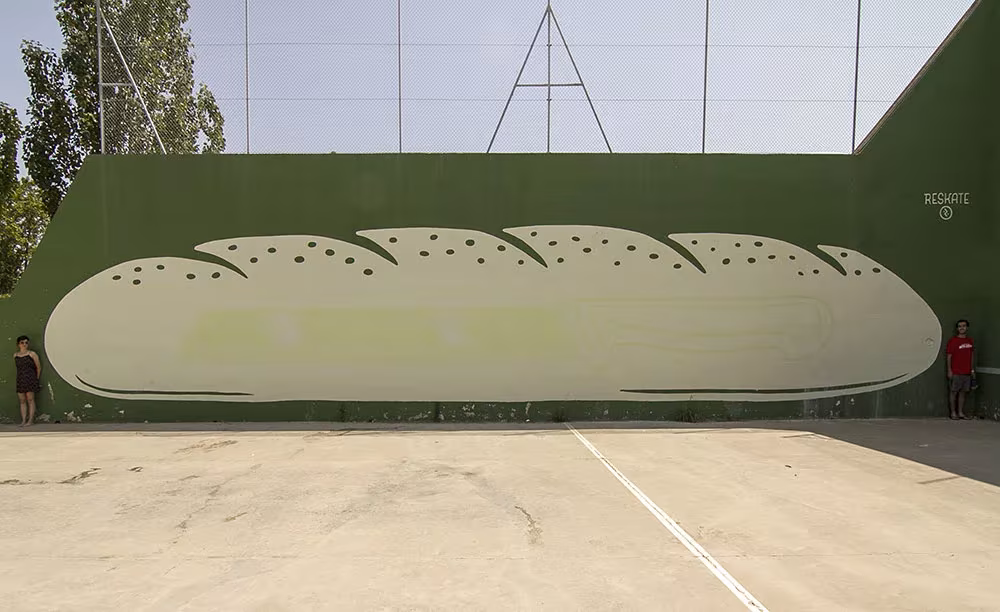 Mural fotoluminiscente con forma de barra de pan sobre un frontón verde del Harreman Project de Reskate
