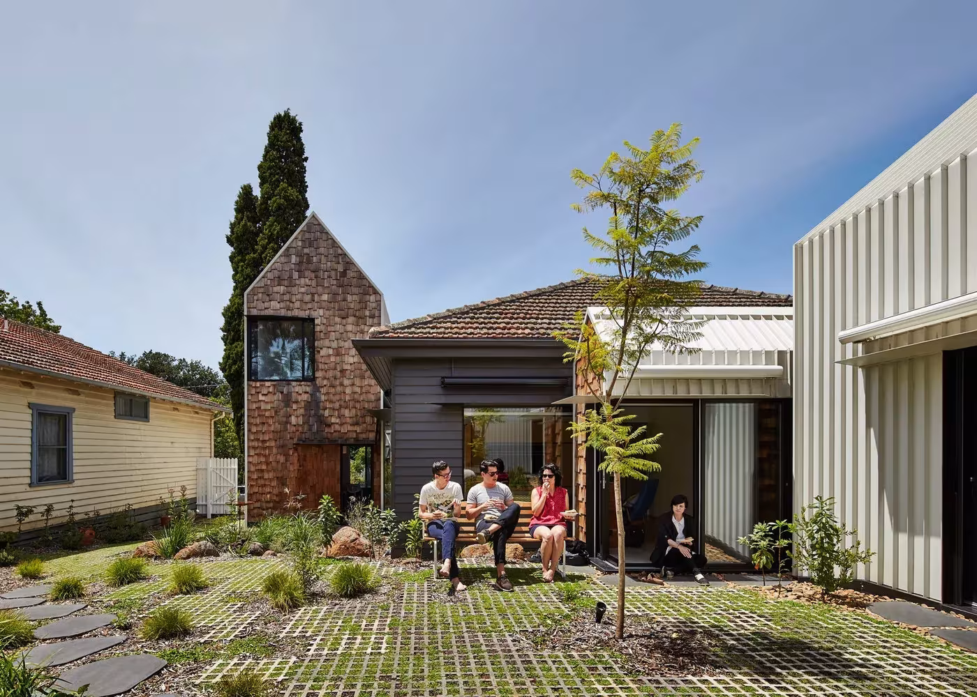 Jardín con losas y gramilla ante las casitas de tejado a dos aguas de la Tower House, en Alphington