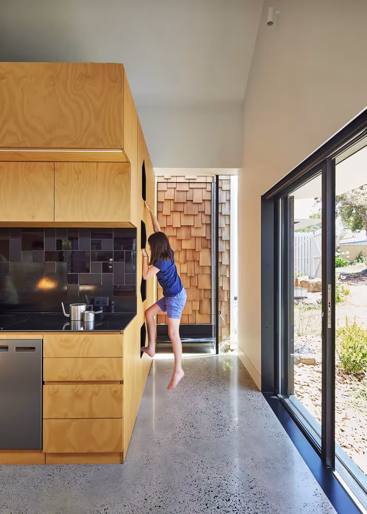Cocina de contrachapado con un volumen escalable y una niña trepando junto a la corredera al jardín en la Tower House