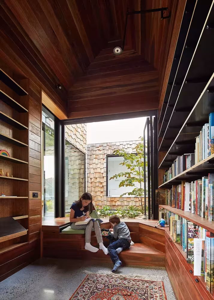 Rincón de lectura con estanterías hasta el techo y ventana-banco abierta al patio en la Tower House de Melbourne