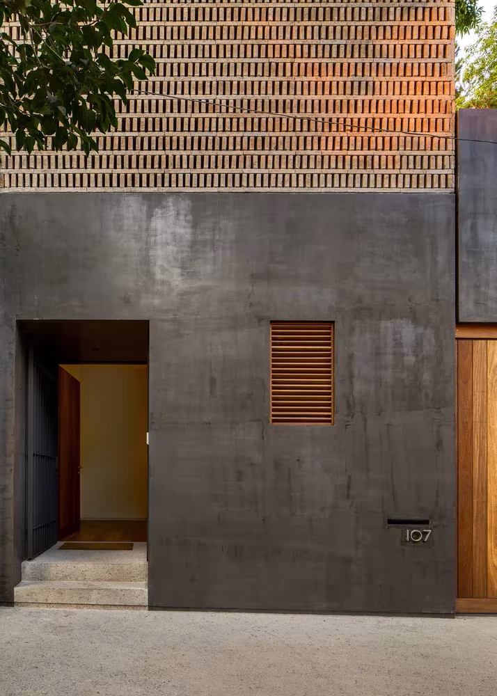 Detalle de la fachada de hormigón con persiana de lamas y puerta de madera bajo la celosía de ladrillo, Casa Campestre