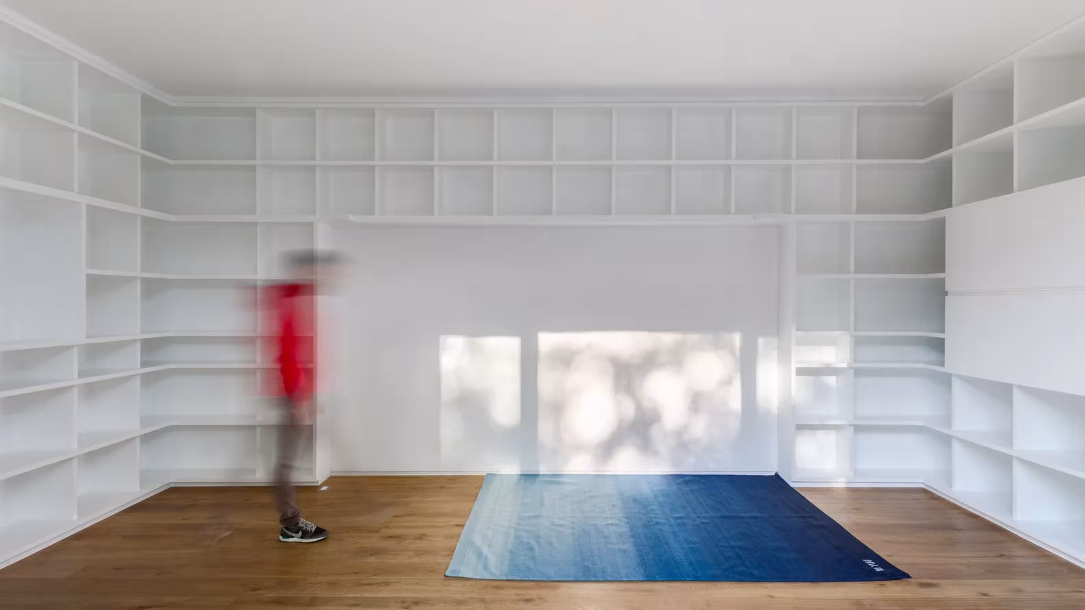 Sala blanca con estanterías empotradas, suelo de madera y una alfombra azul en la Casa Campestre de DCPP Arquitectos