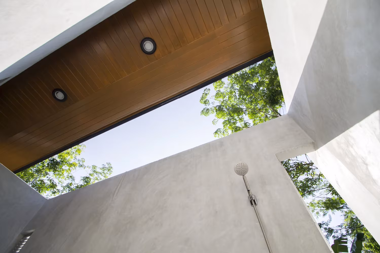 Contrapicado del baño abierto con alero de madera y muros de cemento recortando el cielo, Phatthalung House