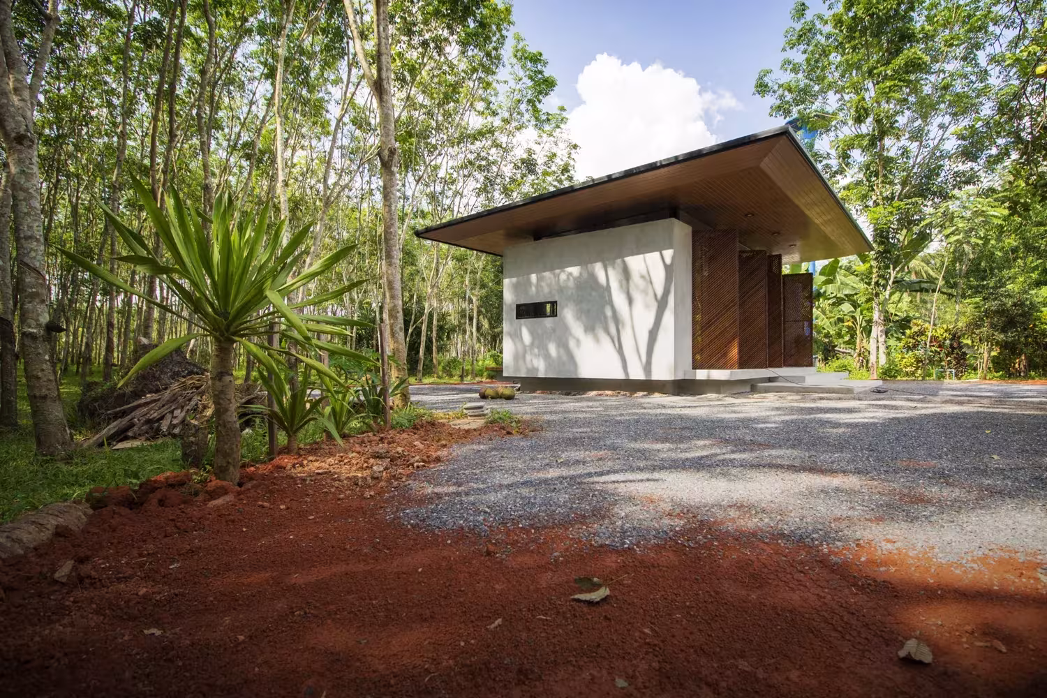 Casa blanca de cubierta inclinada entre palmeras y tierra roja en la plantación de caucho de Phatthalung