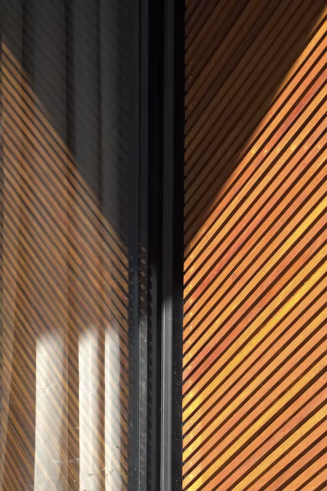 Detalle de lamas de madera diagonales junto a la carpintería negra en la Phatthalung House