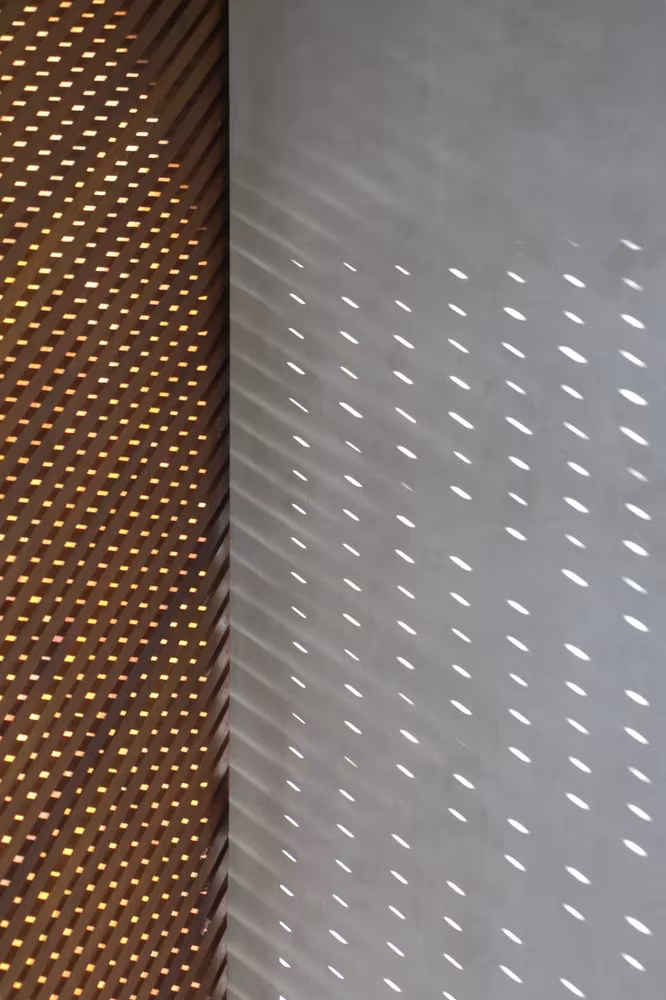 Panel de madera perforado que proyecta puntos de luz sobre el muro blanco en la Phatthalung House