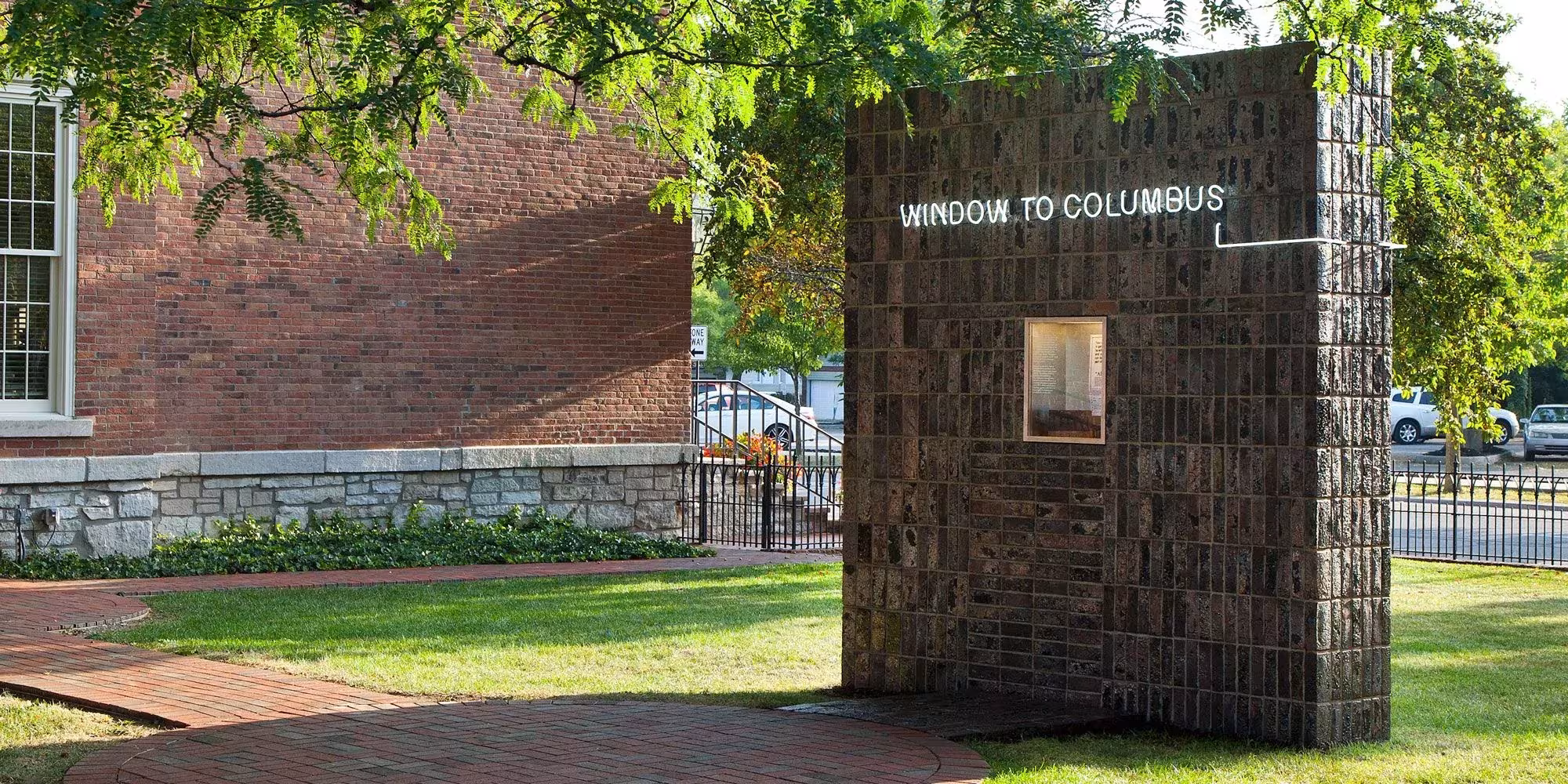 Instalación Window to Columbus de Formafantasma, un muro de ladrillo con una pequeña ventana sobre el césped de un jardín en Columbus