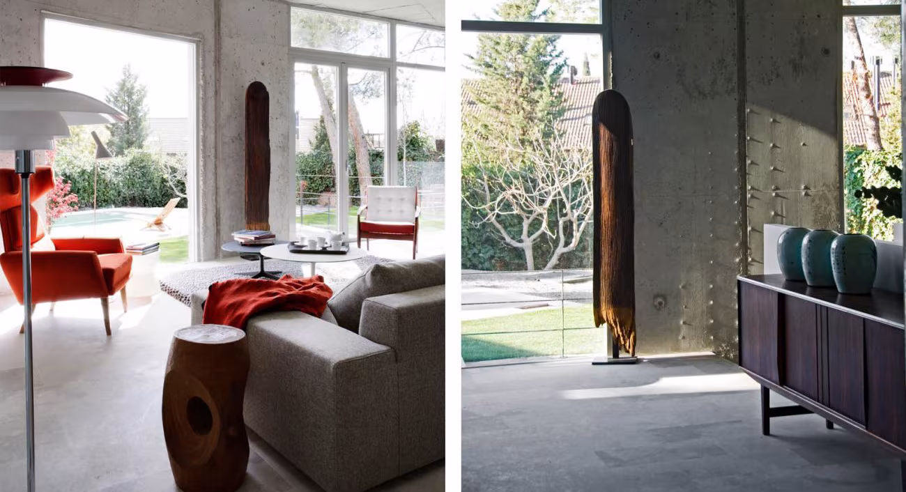 Salón del loft Casa AA con sofá gris y butaca naranja, junto a un aparador oscuro ante una columna de hormigón