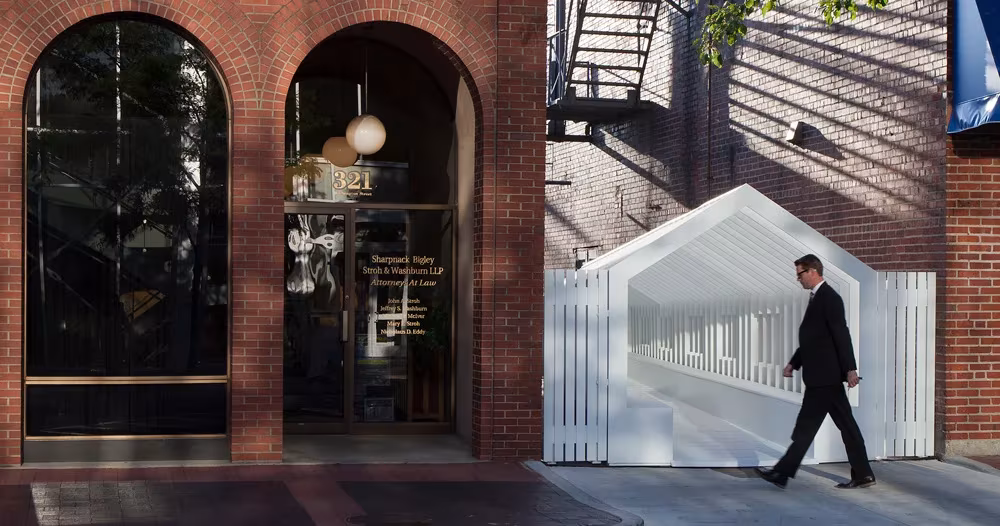 Instalación Playhouse de Snarkitecture, una casa blanca de listones calada junto a una fachada de ladrillo con arcos