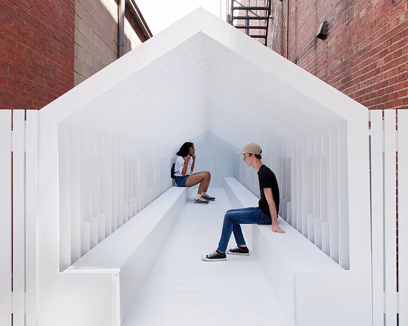 Dos personas sentadas en las gradas blancas del interior de Playhouse de Snarkitecture, con silueta de casa a dos aguas