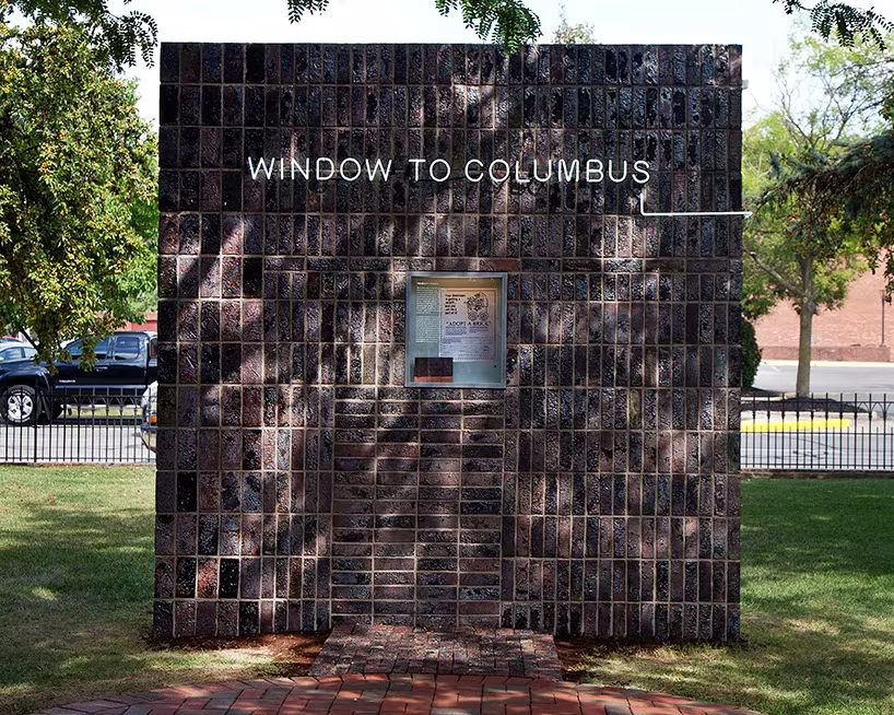 Vista frontal de Window to Columbus de Formafantasma, cubo de ladrillo oscuro con una ventana central sobre el césped