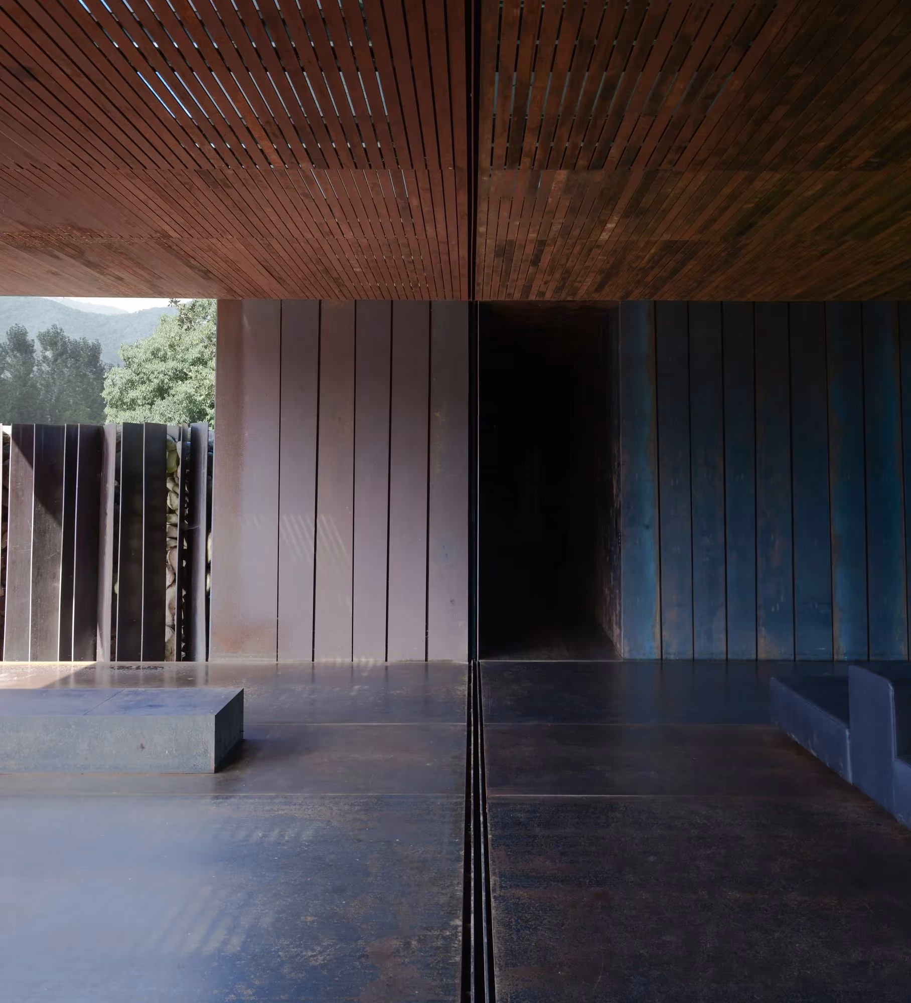 Sala de acero oxidado con techo de madera y bancos de hormigón abierta al paisaje, Casa Horizonte de RCR