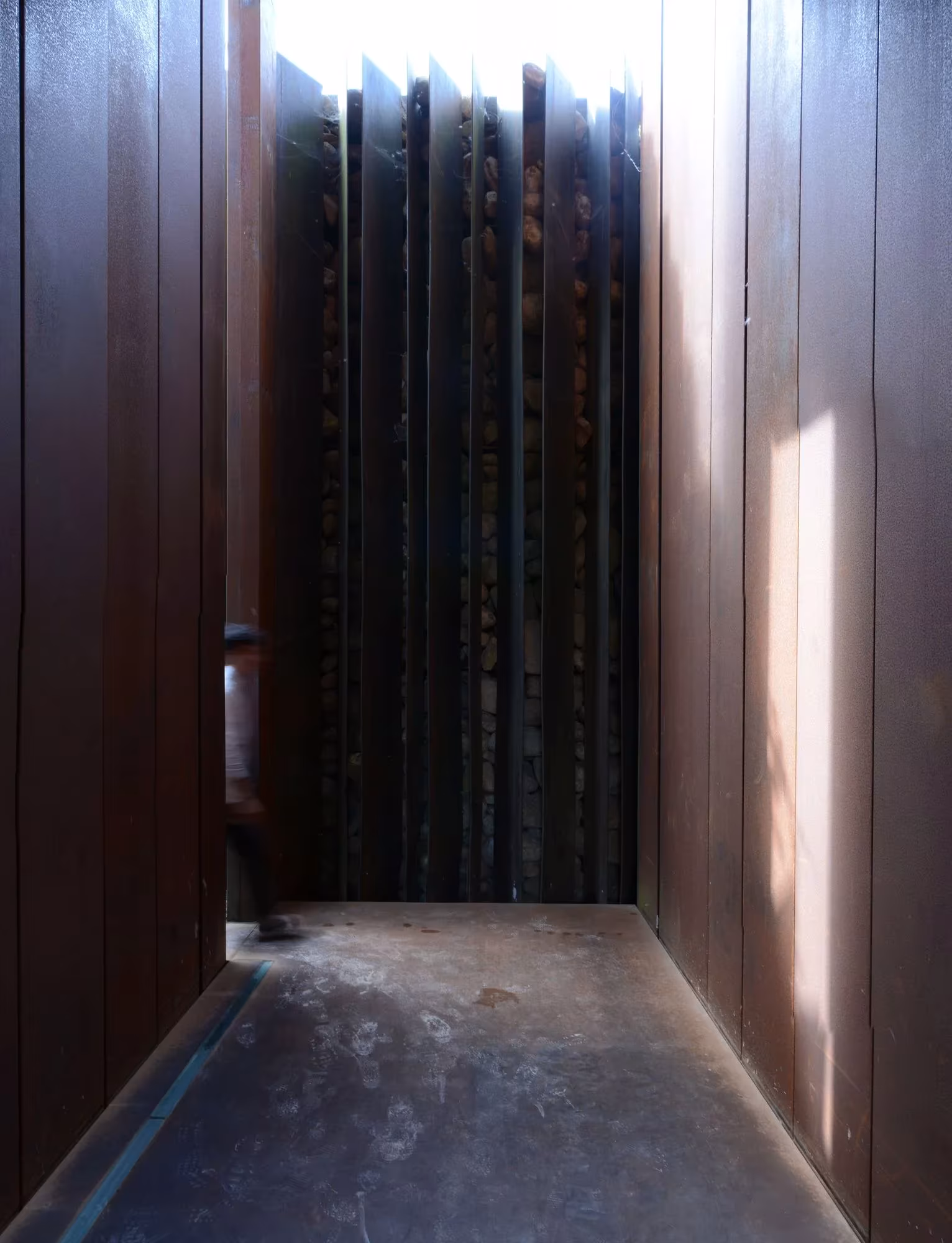 Paso entre planchas verticales de acero corten con luz lateral en la Casa Horizonte de RCR