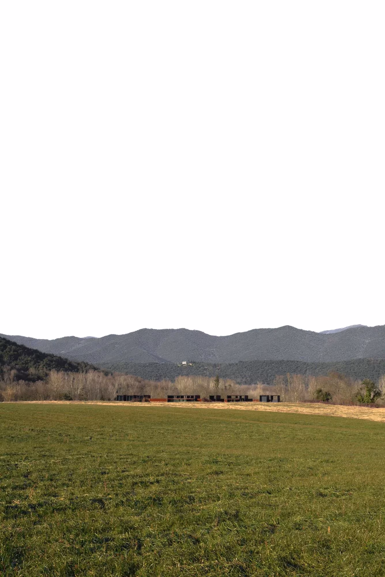 Prado verde ante las montañas con la Casa Horizonte de RCR como una línea oscura en el horizonte