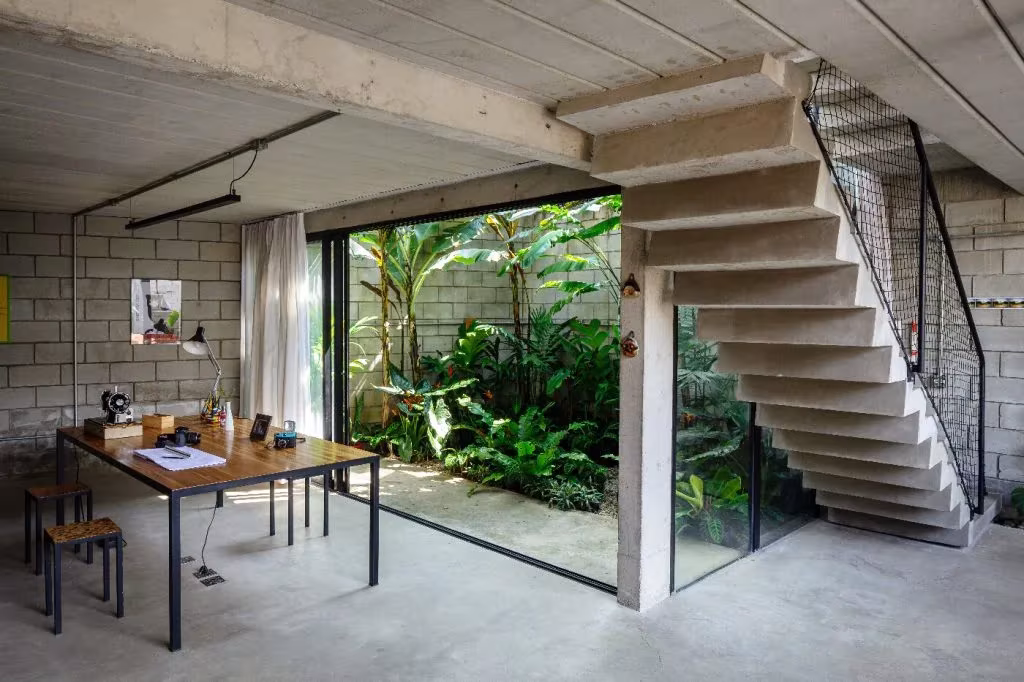 Comedor con mesa de madera junto a una escalera de hormigón volada que da a un jardín interior, Terra e Tuma