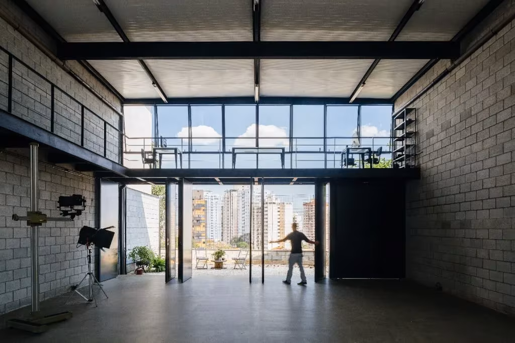 Estudio de doble altura con entreplanta metálica y gran ventanal a la ciudad en la Casa Studio Lapa de Terra e Tuma