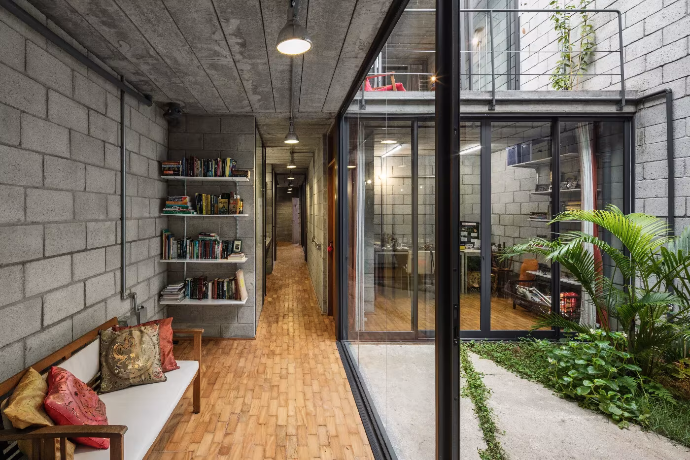 Pasillo de ladrillo y bloque con banco y librería que mira a un jardín interior en una casa de Terra e Tuma