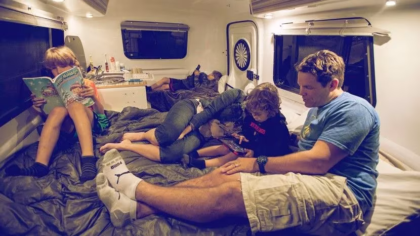 Familia leyendo y descansando sobre la cama del interior de la caravana HC1 de Happier Camper