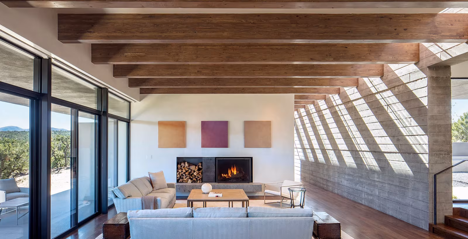 Salón con chimenea bajo vigas de madera y un muro de hormigón rayado por el sol en la Sundial House