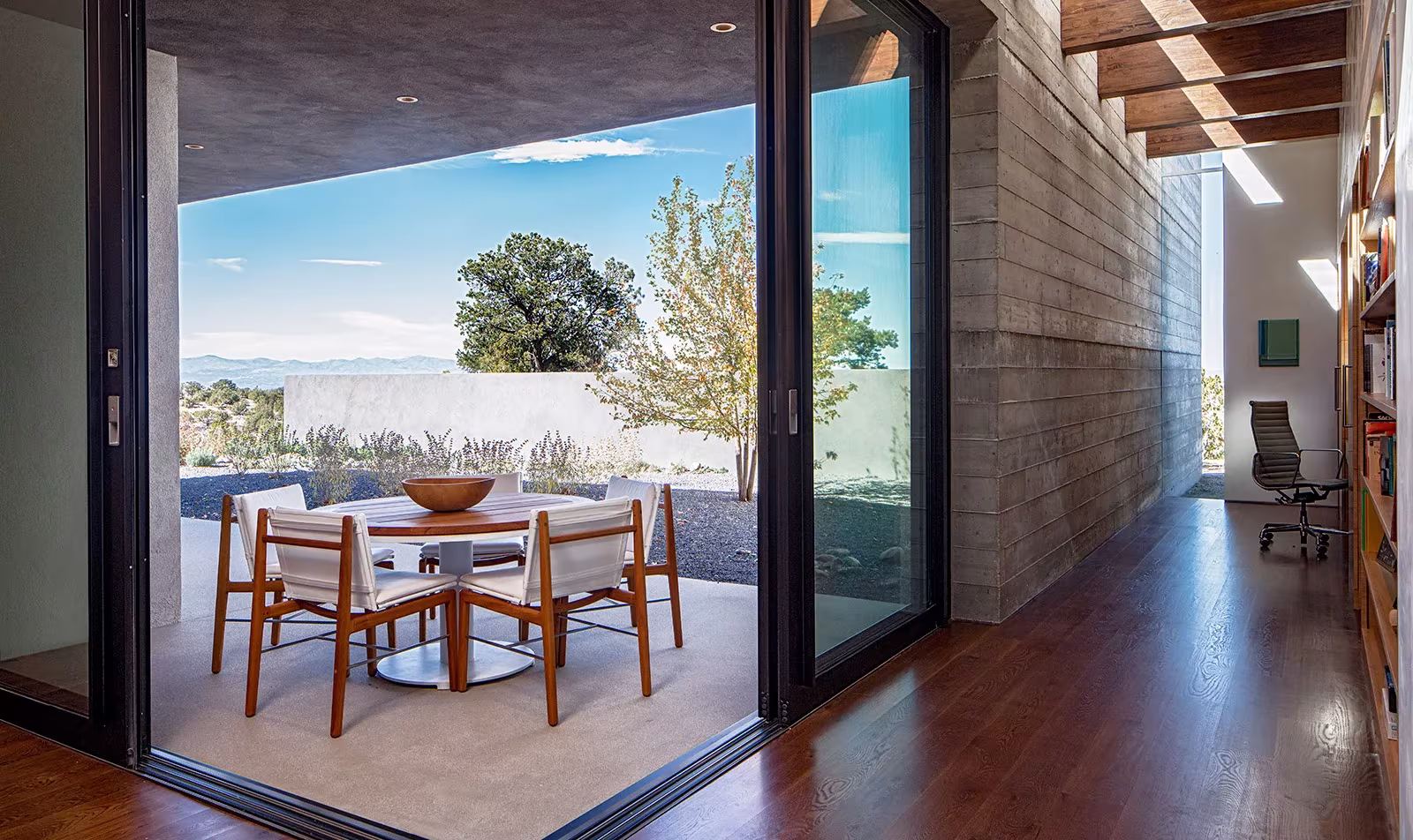 Comedor bajo porche abierto con corredera acristalada junto al muro de hormigón de la Sundial House