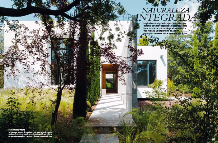 Apertura de Naturaleza integrada en Nuevo Estilo, con el acceso de la casa entre vegetación densa y volúmenes blancos