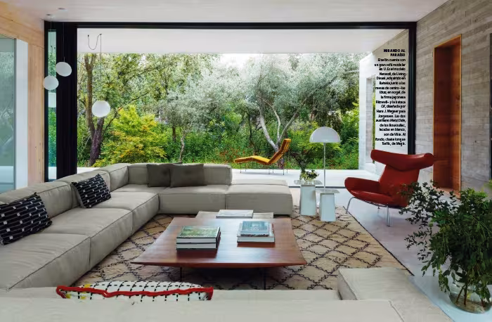 Doble página de Nuevo Estilo con un salón de sofá en L abierto a un jardín frondoso, con butaca roja y alfombra bereber