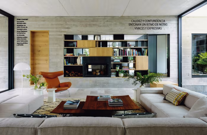 Doble página de Nuevo Estilo con un salón de hormigón visto, librería oscura, sofás y butaca de cuero junto a un gran ventanal